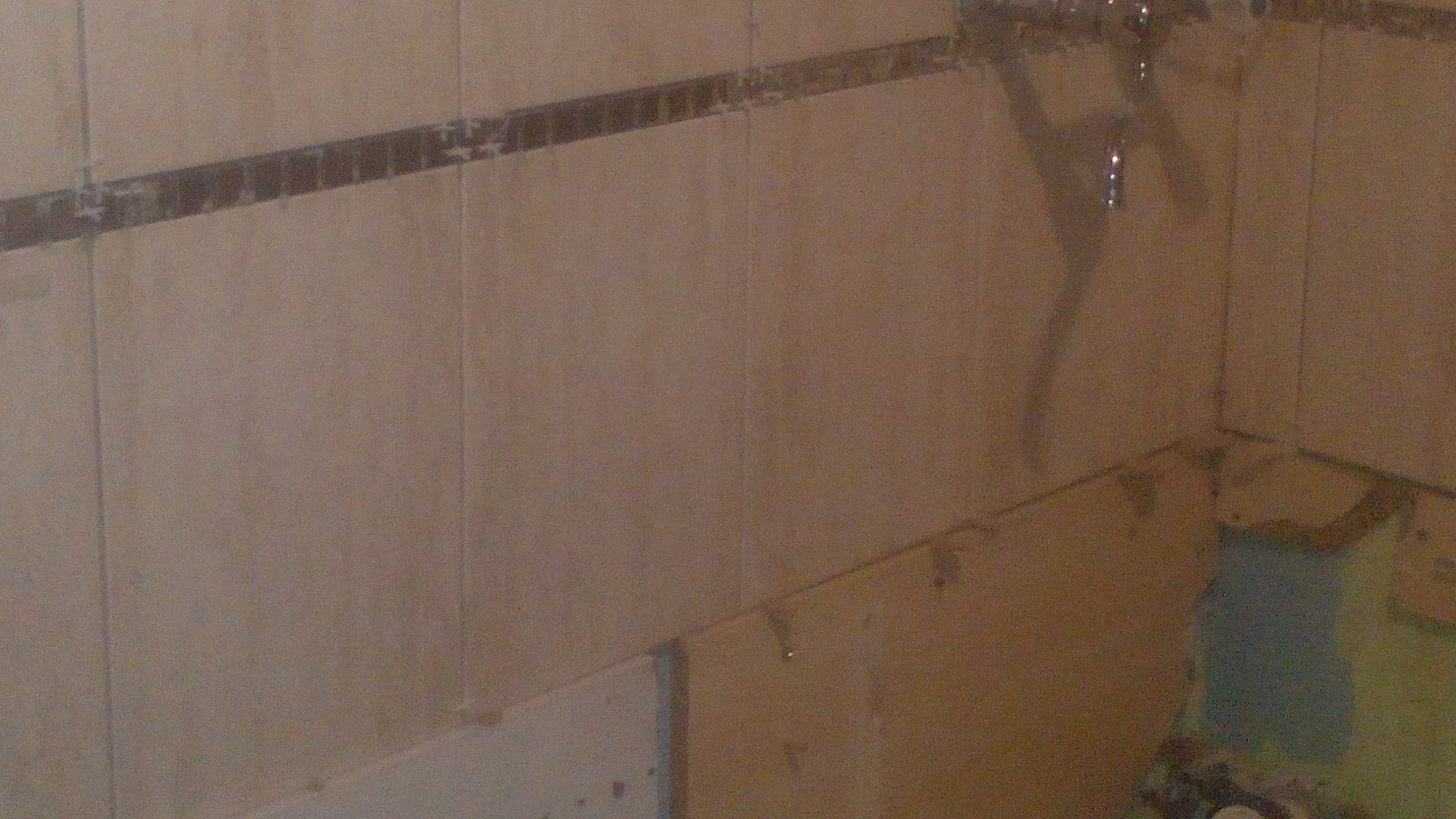 Ściana w trakcie układania płytek ceramicznych, widoczne krzyżyki dystansowe i fragment niezabezpieczonej ściany w dolnym rogu.