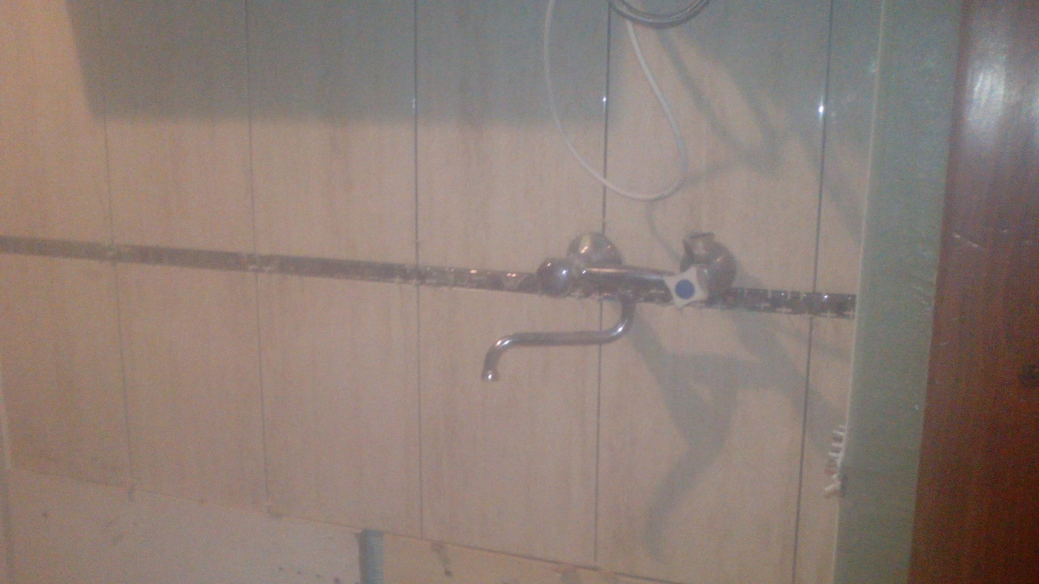 Stara bateria umywalkowa zamontowana na ścianie wyłożonej płytkami, widoczne ślady po wcześniejszym montażu i niedokładne fugowanie.