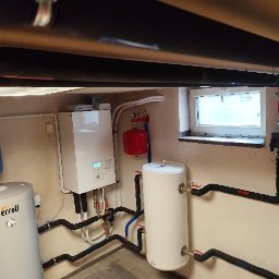 Gedeon Wróblewski Sp.j - Zestaw urządzeń grzewczych w kotłowni: zbiornik Ferroli, piec gazowy, naczynia przeponowe, orurowanie z izolacją termiczną, okno w tle.