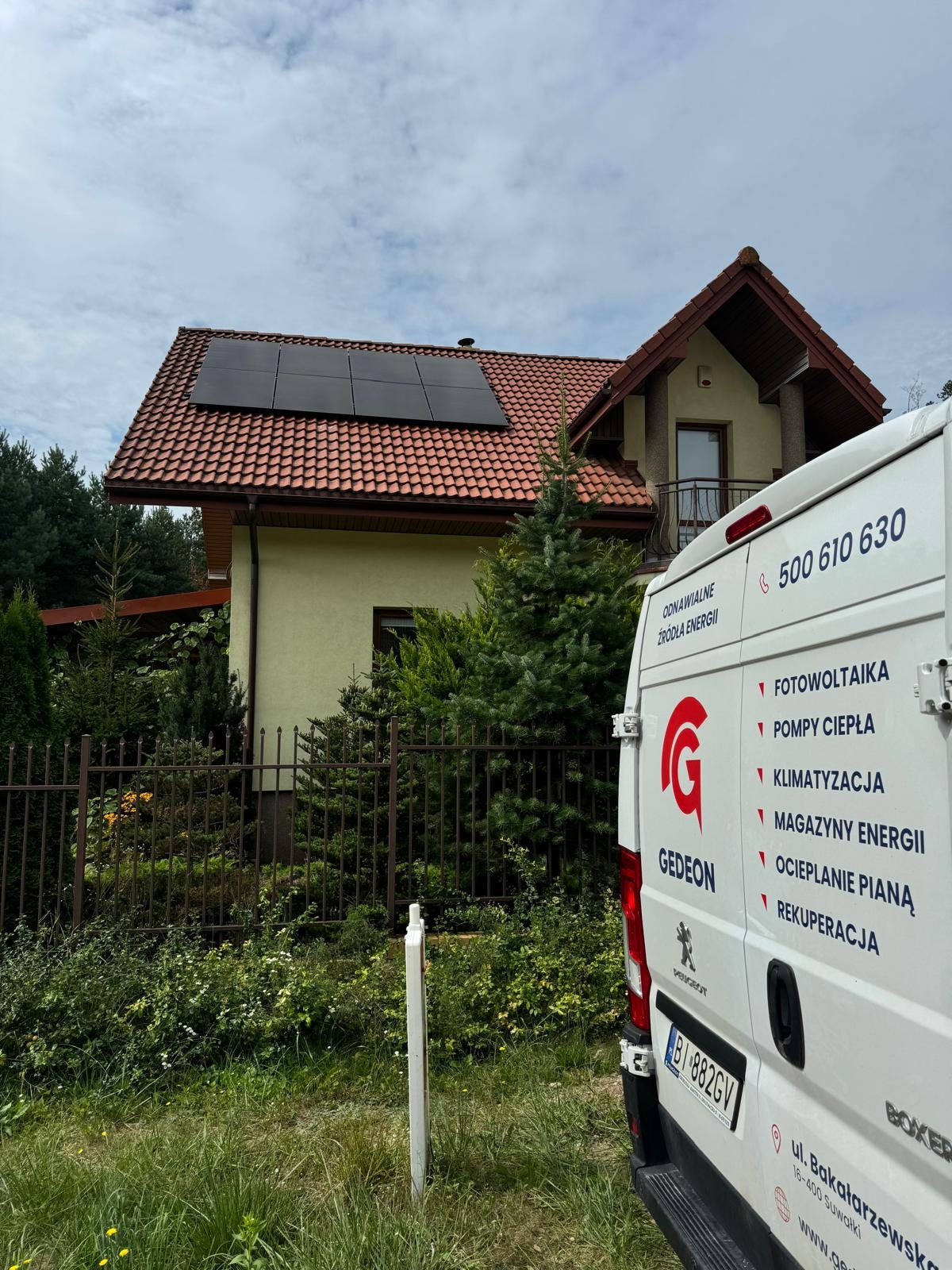 Dom jednorodzinny z panelami słonecznymi na dachu, widok zza firmowego samochodu z logo 'Gedeon' i listą usług: fotowoltaika, pompy ciepła, klimatyzacja, magazyny energii, ocieplanie pianą...