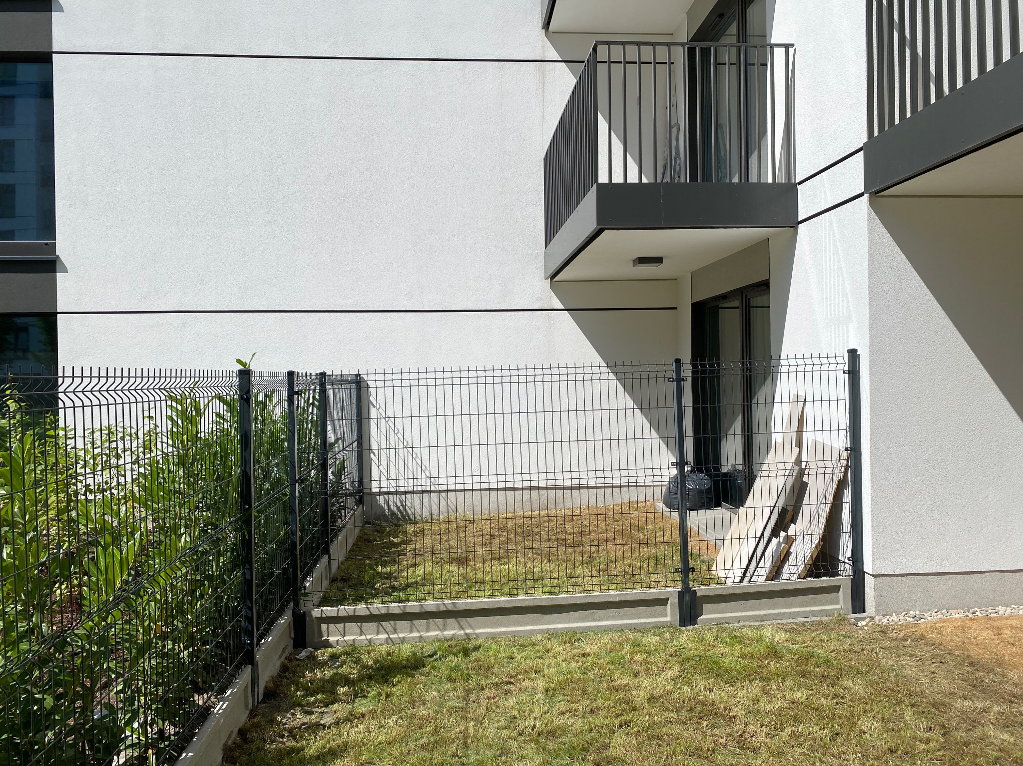 Nowoczesne ogrodzenie panelowe w Śladów, z podmurówką, na tle białej elewacji budynku z balkonami. Widoczne elementy montażowe i trawnik.