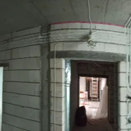 Wnętrze surowego mieszkania w trakcie prac remontowych z widocznymi przewodami elektrycznymi ułożonymi wzdłuż ścian i sufitu, przygotowanymi do dalszego rozprowadzenia.