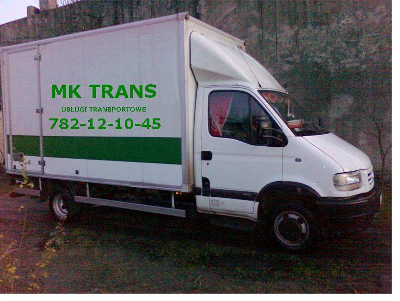 Biały samochód dostawczy z zielonym pasem i napisem 'MK TRANS USŁUGI TRANSPORTOWE 782-12-10-45' zaparkowany na trawie, widok z boku na tle betonowego muru.