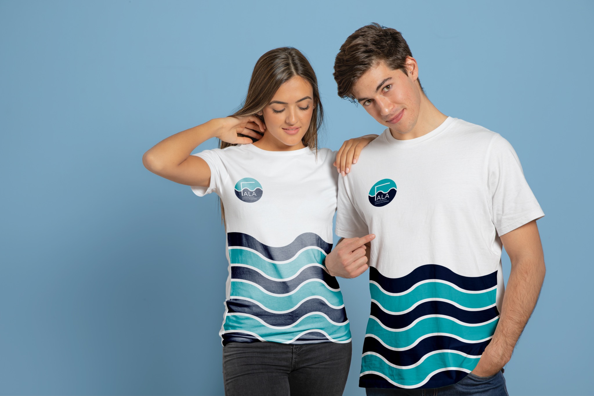 Dwoje młodych ludzi pozuje w białych koszulkach z nadrukowanym logo i motywem fal na błękitnym tle.