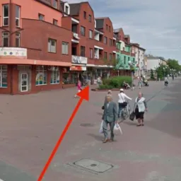 Ulica miejska z budynkami z czerwonej cegły, chodnikiem z kostki brukowej i przechodzącymi pieszymi w słoneczny dzień.