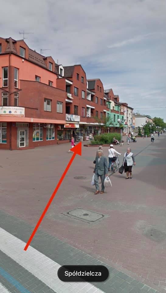 Ulica miejska z budynkami z czerwonej cegły, chodnikiem z kostki brukowej i przechodzącymi pieszymi w słoneczny dzień.