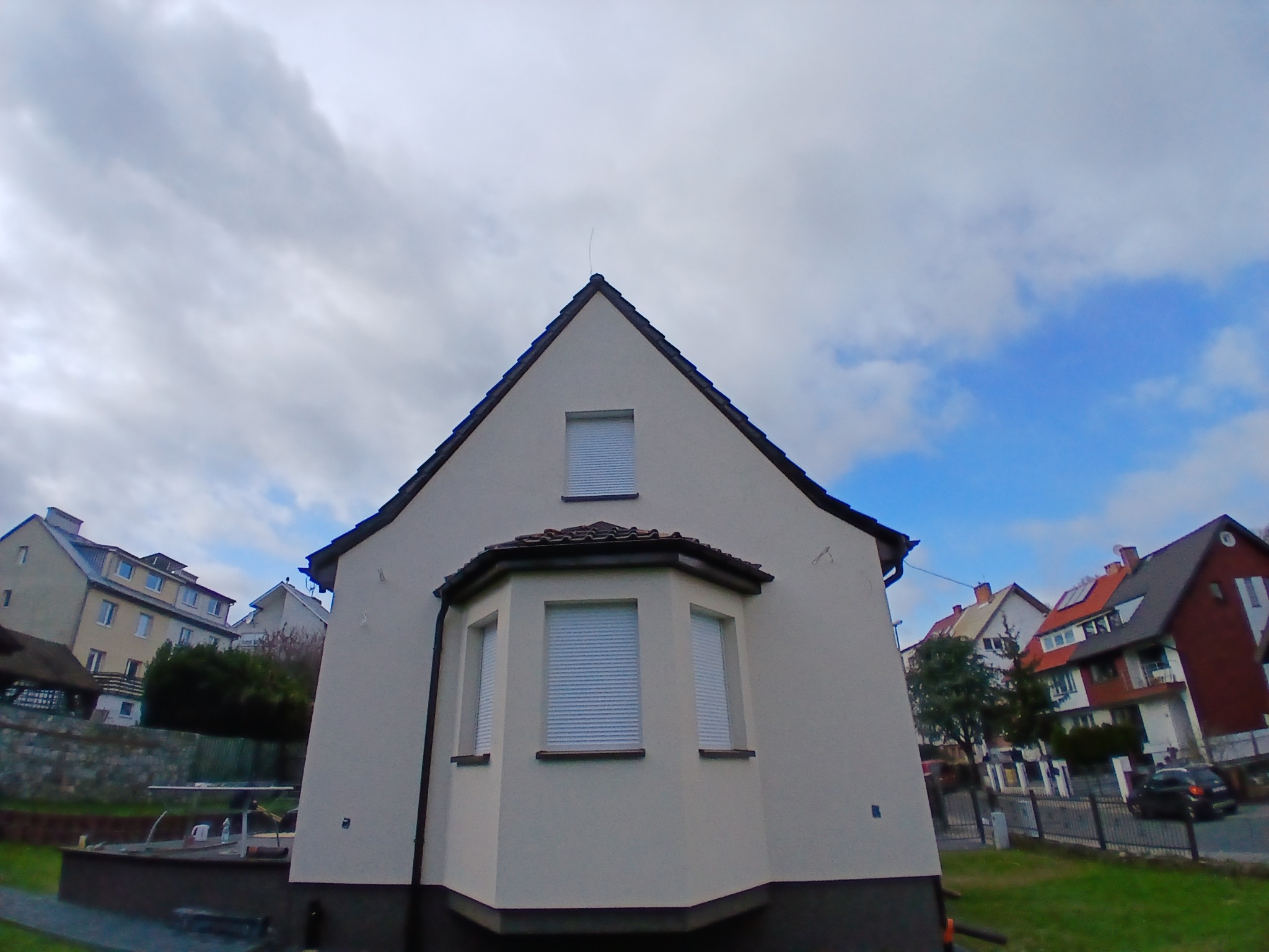 Elewacja domu jednorodzinnego z oknami z roletami zewnętrznymi, widok z dołu na tle pochmurnego nieba.