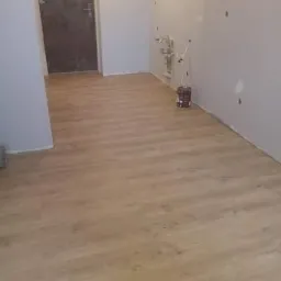 Układanie paneli podłogowych w pomieszczeniu w trakcie remontu w Żelechowie, widoczna puszka farby i instalacja wodna na ścianie.