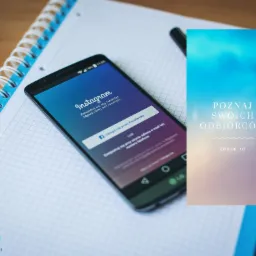 Smartfon wyświetlający ekran logowania do Instagrama, leżący na notesie w kratkę obok ulotki reklamowej z napisem 'Poznaj swoich odbiorców' i logo Dream Ad.