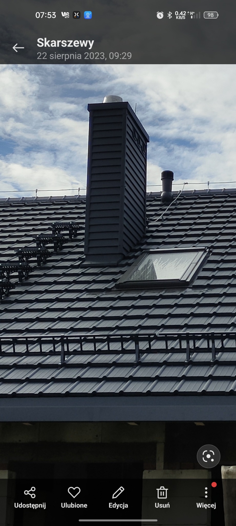 Grafitowy dach z dachówki ceramicznej z oknem połaciowym i kominem w nowoczesnym stylu. Widoczne zabezpieczenia przeciwśniegowe.