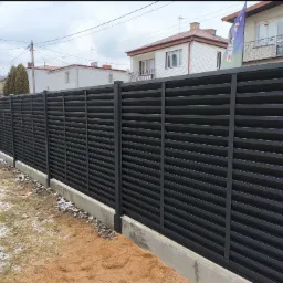 Nowoczesne, poziome, grafitowe ogrodzenie panelowe na betonowej podmurówce, widok z zewnątrz posesji, z elementami trawnika i śniegu.