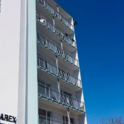 Wysoki budynek mieszkalny w Stargardzie z balkonami zabezpieczonymi metalowymi barierkami, widok z dołu na tle błękitnego nieba.