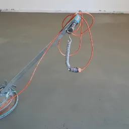 Zacieraczka mechaniczna marki KREBER w trakcie pracy na świeżo wylanym, szarym podkładzie podłogowym w jasnym pomieszczeniu.