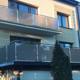 Elewacja budynku z dwoma balkonami zabezpieczonymi szklanymi panelami w stalowych ramach, widoczne numery adresowe 73A i 75.