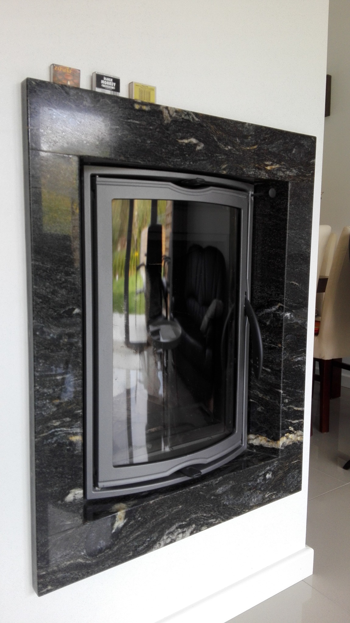 Zamknięty wkład kominkowy z obudową z ciemnego granitu, na górnej krawędzi wkładu leżą trzy pudełka zapałek.