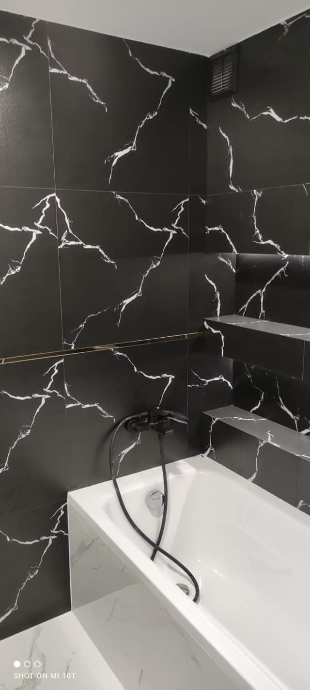 Wykończona łazienka z czarnymi płytkami imitującymi marmur, białymi elementami armatury i półkami z tego samego materiału co płytki.