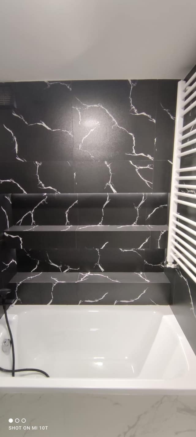 Nowoczesna łazienka z czarnymi płytkami imitującymi marmur, biała wanna i grzejnik drabinkowy