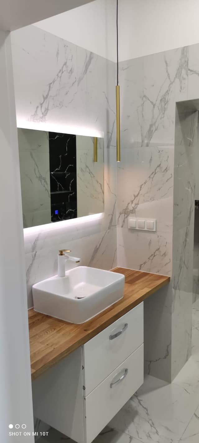 Nowoczesna łazienka z umywalką nablatową na drewnianym blacie, podświetlanym lustrem i marmurowymi płytkami.