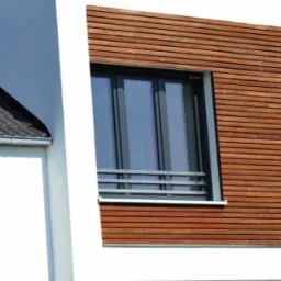 Nowoczesny dom z białymi ścianami i drewnianą elewacją, z zamontowanymi oknami o grafitowych ramach i metalowymi barierkami pod jednym z nich.