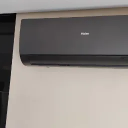 Czarna klimatyzacja Haier zamontowana na beżowej ścianie, obok ściany wykończonej czarnymi, błyszczącymi płytkami.