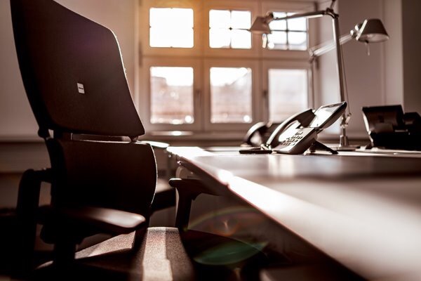 Biuro z krzesłem, biurkiem, telefonem i lampą na tle okna w słoneczny dzień, widok z niskiej perspektywy.