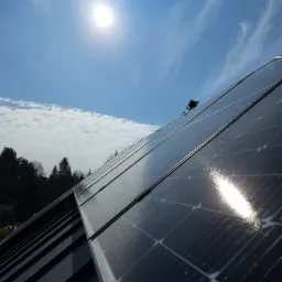 Błyszczące panele słoneczne na dachu metalowym w słoneczny dzień z chmurami, widok pod kątem.