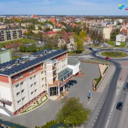 Widok z g&oacute;ry na budynek z panelami słonecznymi na dachu, z rondem i zabudową miejską w tle.