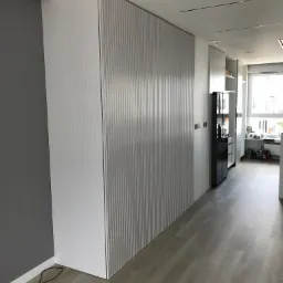 Nowoczesna szafa wnękowa z ryflowanymi frontami w odcieniach bieli i szarości, dopasowana do wnętrza mieszkania w Ełku, widoczna z perspektywy korytarza z jasną podłogą.