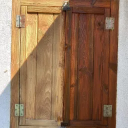 Drewniana okiennica dwuskrzydłowa, połowa po renowacji z widoczną r&oacute;żnicą w kolorze drewna, jasny odcień po lewej, ciemny po prawej.