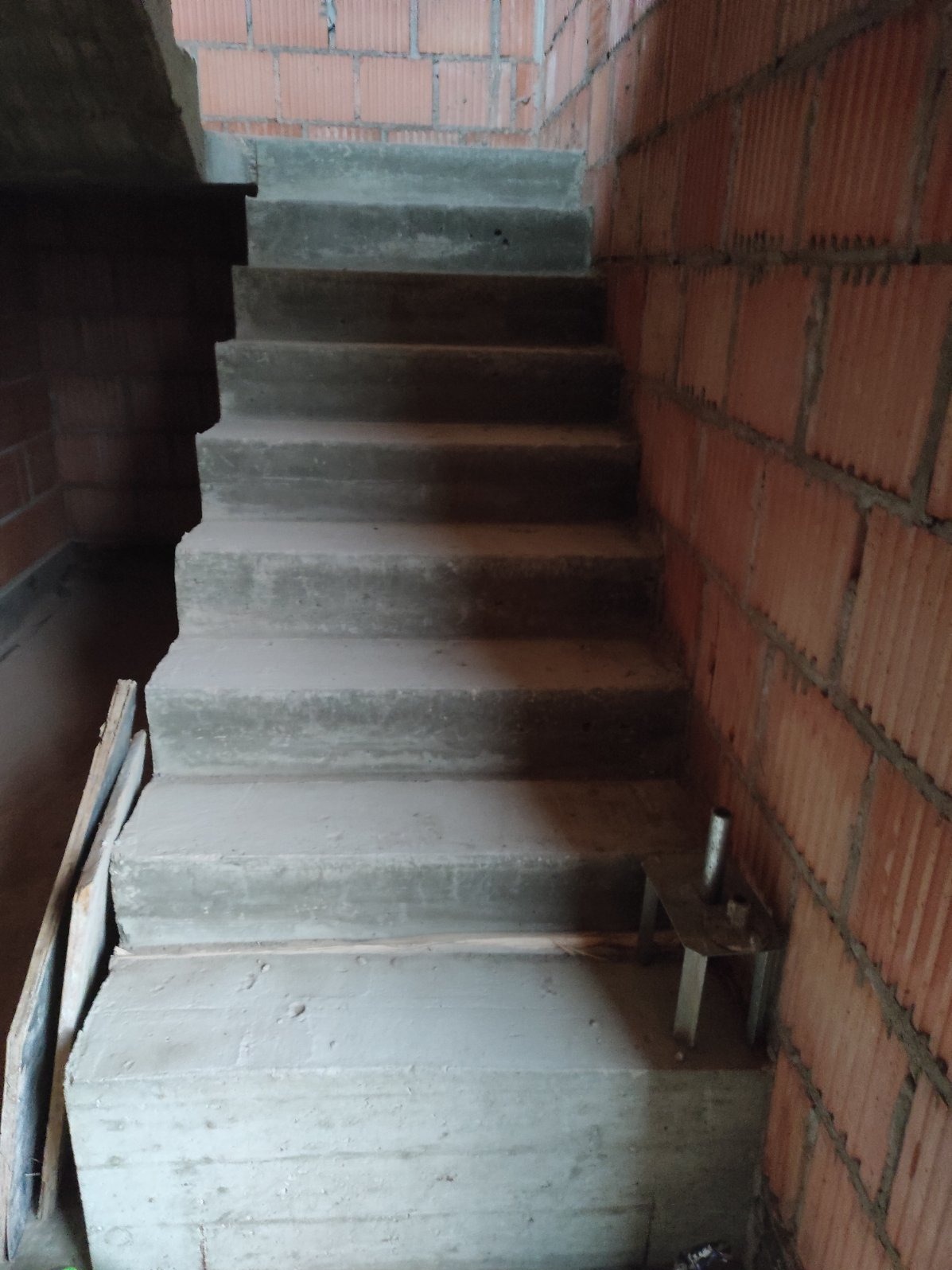Surowe, betonowe schody wewnętrzne w trakcie budowy domu, widoczne czerwone, murowane ściany z pustaków.