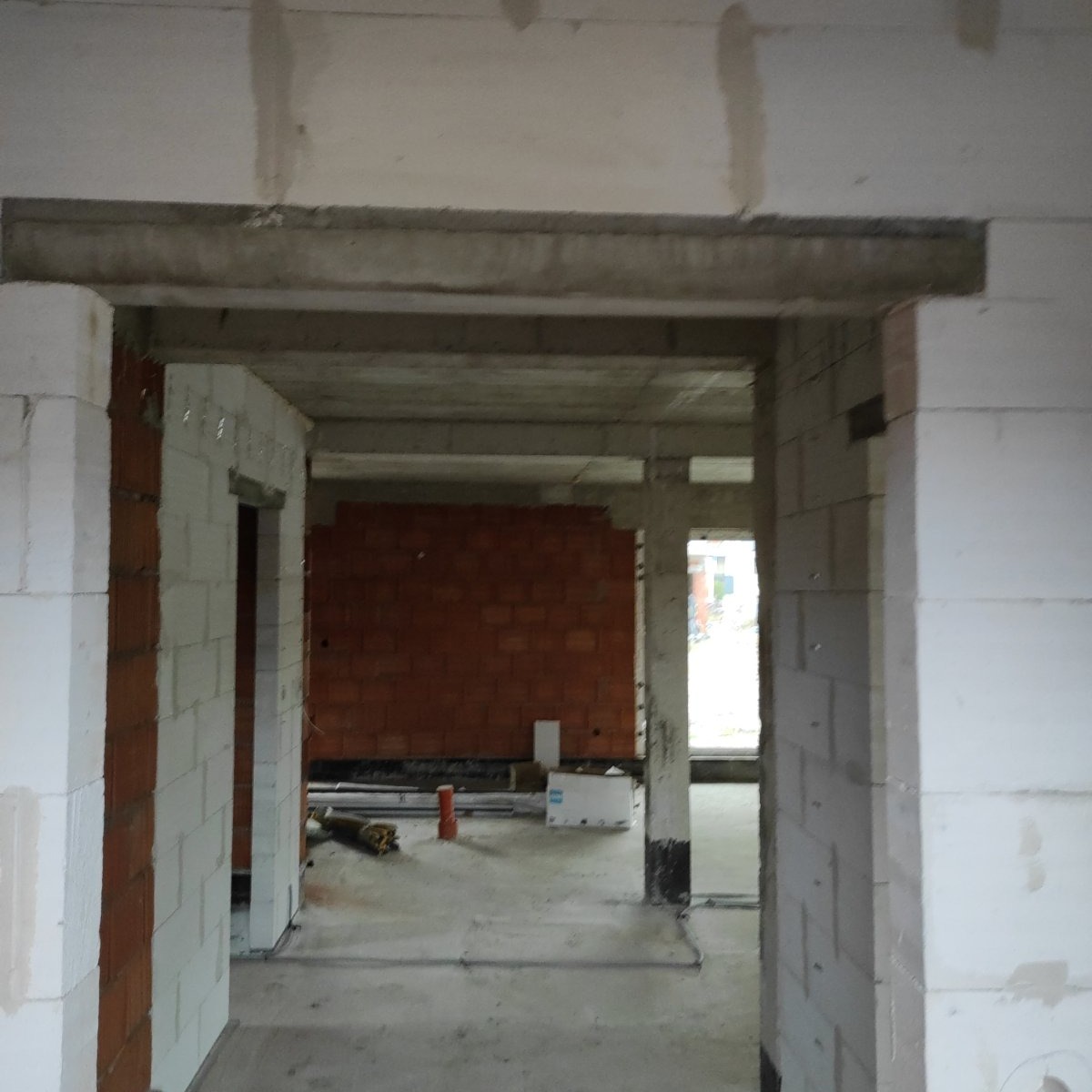 Wnętrze surowego domu w trakcie budowy, widoczne ściany z białych bloczków silikatowych i czerwonej cegły, betonowy strop, elementy instalacji na podłodze.