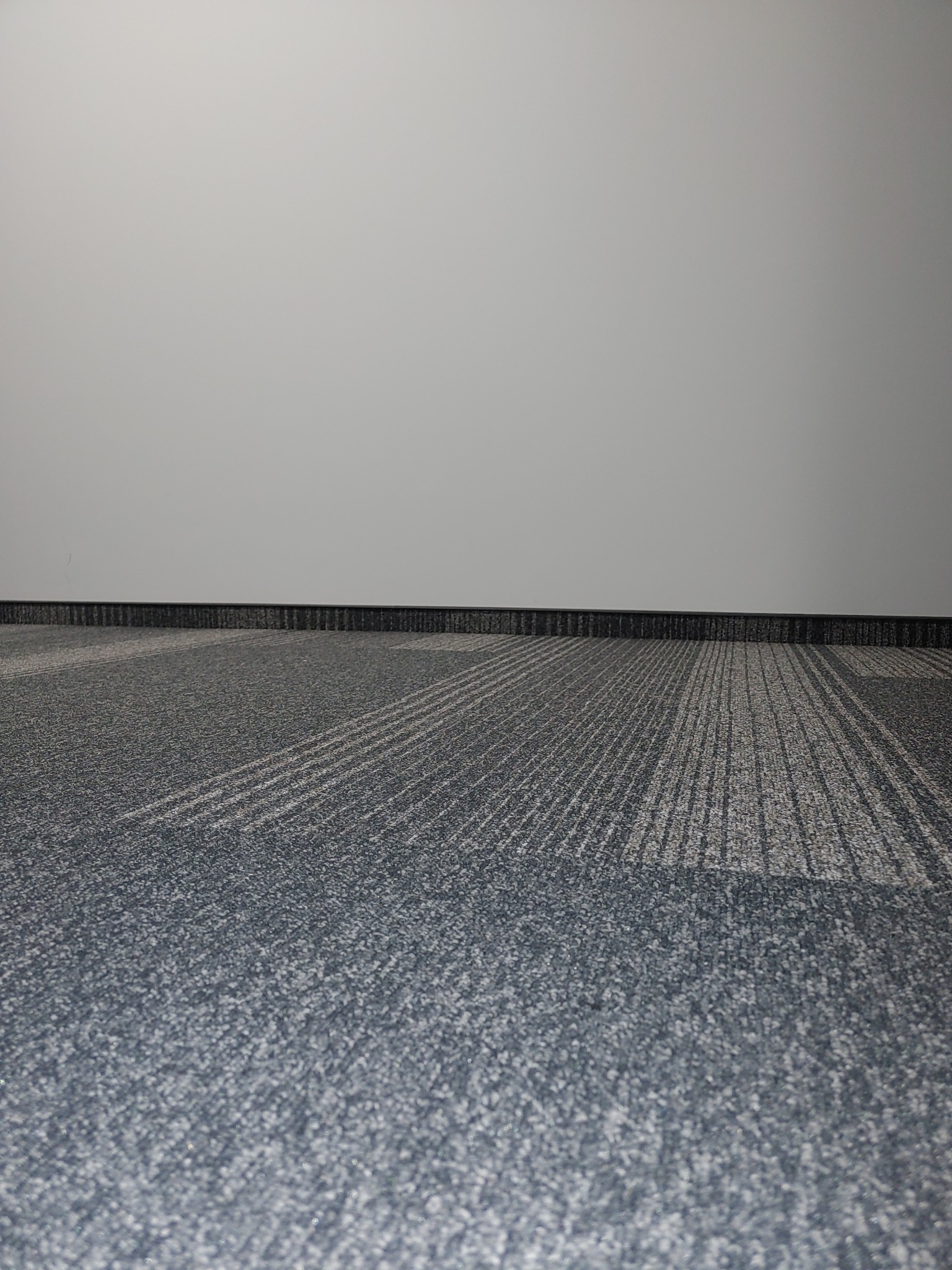Szara wykładzina dywanowa w biurze w Żyrardowie, widok z niskiego kąta, z widoczną listwą przypodłogową i fragmentem ściany w tle.