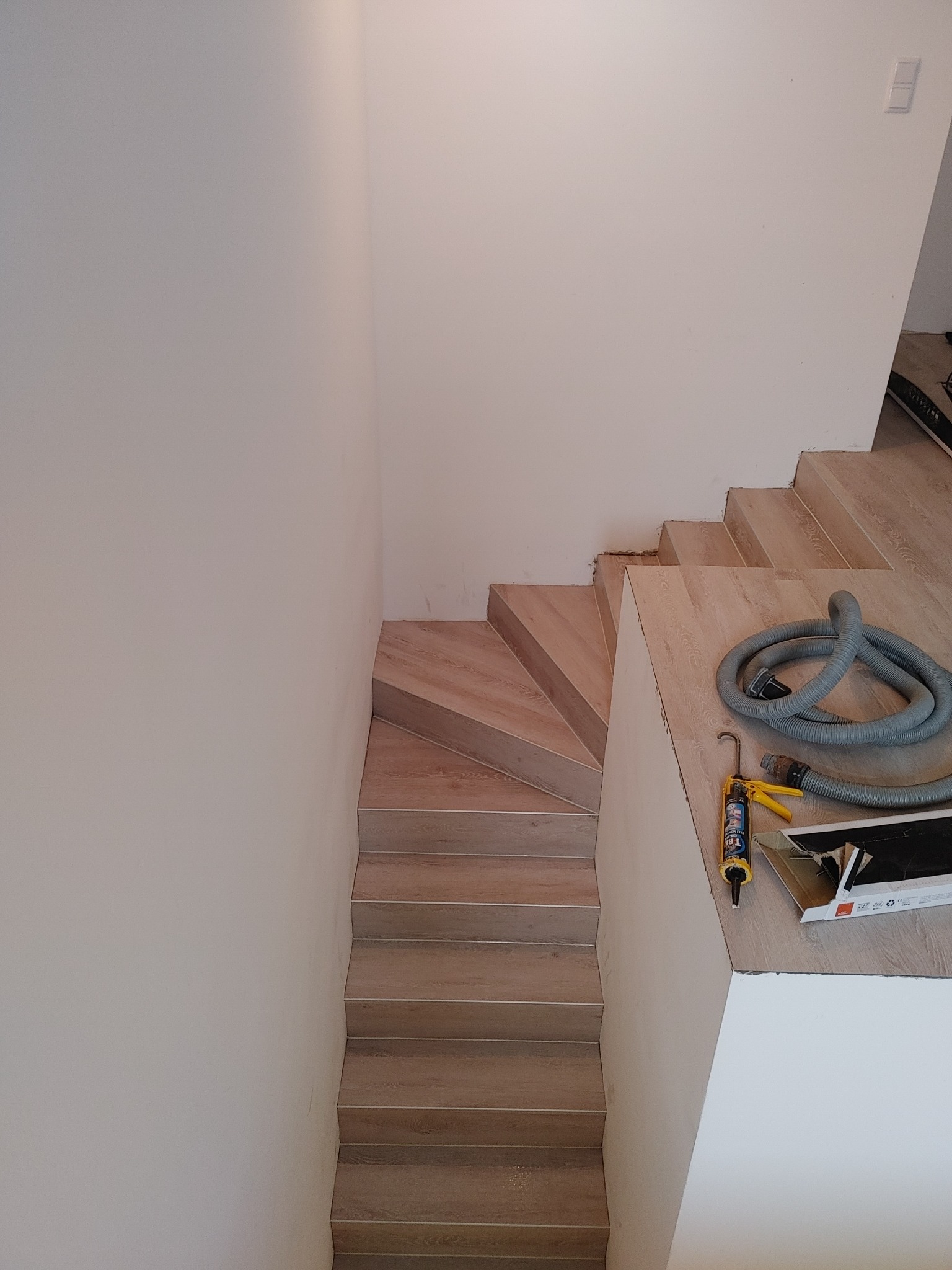 Schody wyłożone panelami imitującymi drewno, widok z góry, obok leżą narzędzia: tuba z klejem i wąż od odkurzacza.