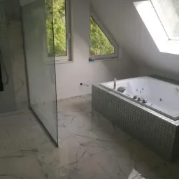 Nowoczesna łazienka na poddaszu z marmurową posadzką, kabiną prysznicową typu walk-in z czarnym panelem natryskowym i wanną z hydromasażem obudowaną mozaiką.