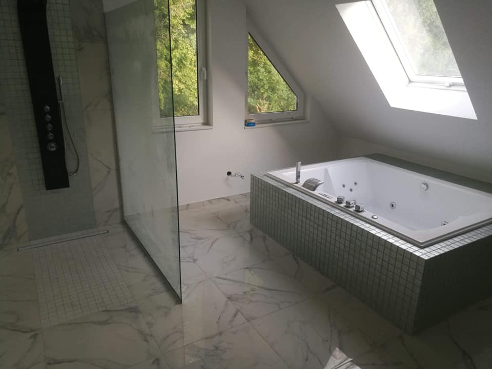 Nowoczesna łazienka na poddaszu z marmurową posadzką, kabiną prysznicową typu walk-in z czarnym panelem natryskowym i wanną z hydromasażem obudowaną mozaiką.