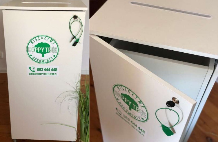 Biała, zamykana szafka na dokumenty z otworem wrzutowym u góry, oznaczona zielonym logo 'Happy Tree' i numerem telefonu, z widocznym zamkiem zabezpieczającym i uchylonymi drzwiczkami ukazującymi...