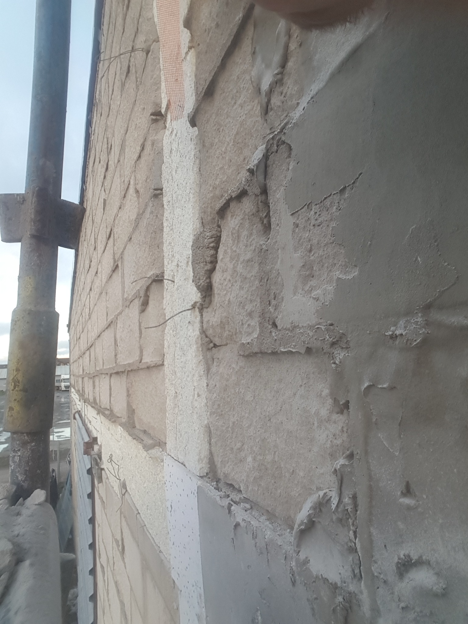 Elewacja budynku w trakcie prac: fragment ściany z widocznym ociepleniem, siatką i częściowo nałożonym tynkiem, rusztowanie z boku kadru, nierównomierne rozprowadzenie zaprawy.