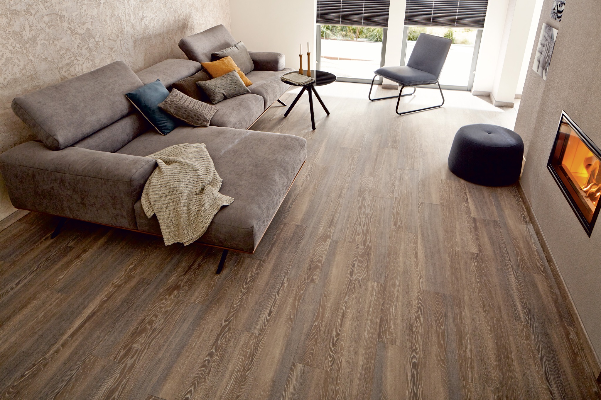 Jasnobrązowa podłoga z paneli drewnopodobnych w salonie z szarym narożnikiem, czarnym stolikiem kawowym i kominkiem w ścianie.