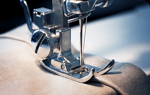 Detal maszyny do szycia z igłą w trakcie pracy na jasnym materiale, widoczne metalowe elementy i precyzyjne szwy.