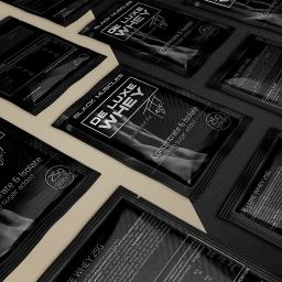 Krasovski.pl - Rozłożone próbki czarnych, matowych saszetek z odżywką białkową Black Muscles De Luxe Whey, ułożone pod kątem na ciemnoszarym tle, eksponujące logo i informacje o wartościach odżywczych.