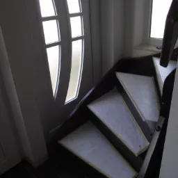 Kątowe ujęcie fragmentu klatki schodowej z ciemnego drewna, stopnie zabezpieczone papierem, widoczna balustrada i drzwi z szybami.