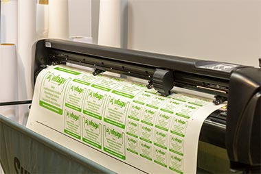 Plotter tnący arkusz naklejek w drukarni w Krakowie. Naklejki z zielonym motywem roślinnym, powtarzające się w regularnych odstępach.