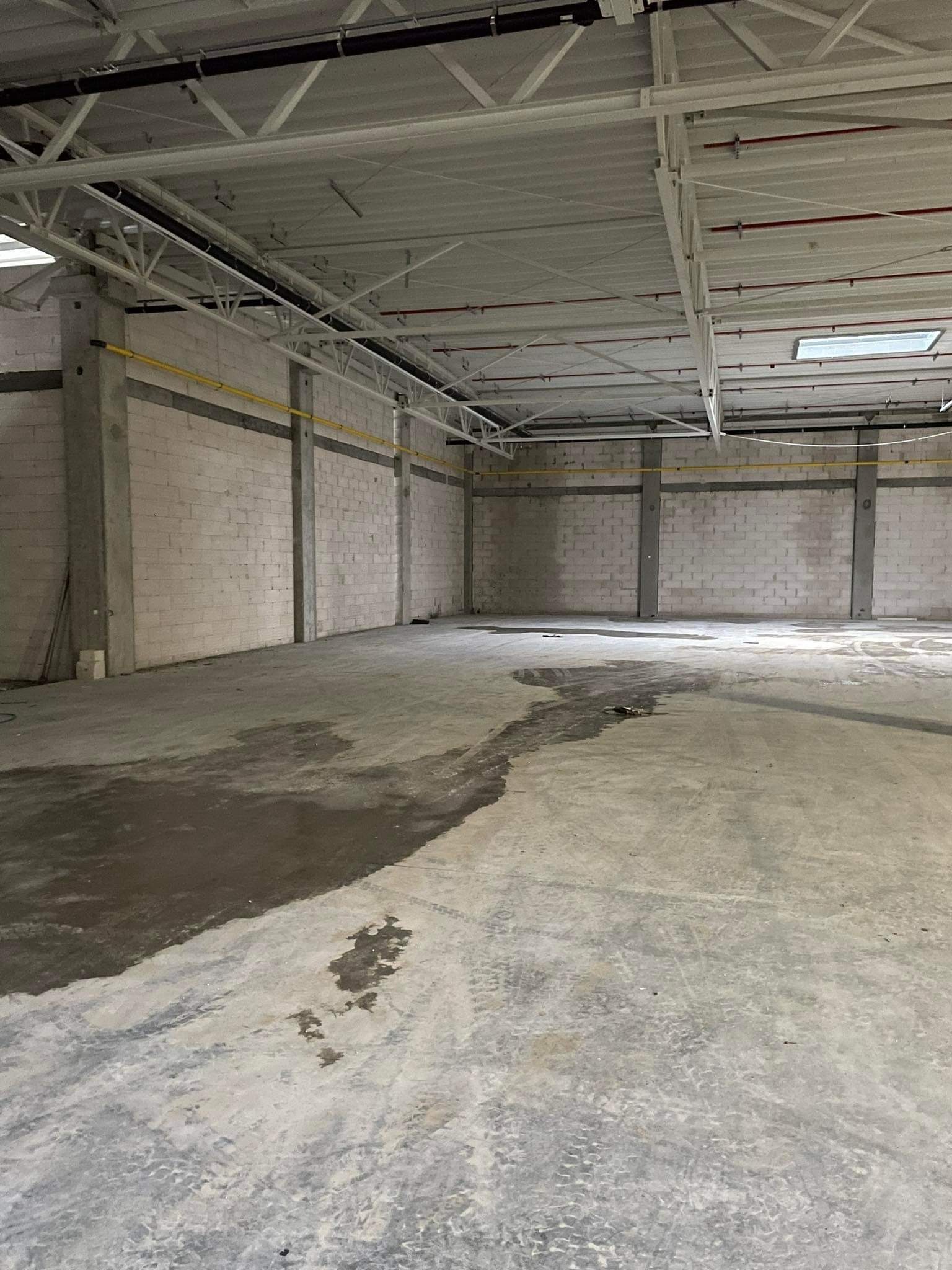 Surowe wnętrze hali magazynowej z betonową posadzką, ścianami z bloczków i odsłoniętą konstrukcją stalową pod sufitem.