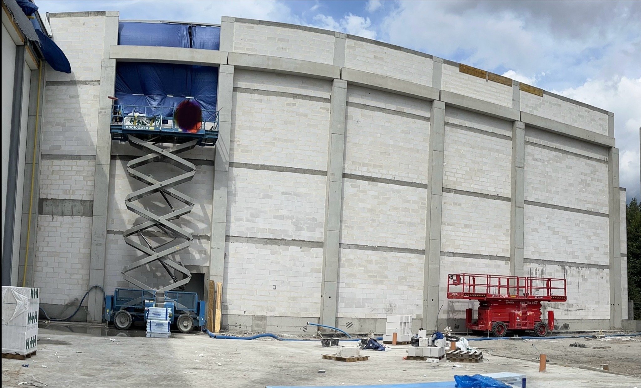 Wznoszenie ściany z bloczków betonowych z użyciem podnośników nożycowych na placu budowy w słoneczny dzień.