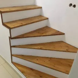 Schody drewniane o trójkątnych stopniach, pomalowane na biało ściany, widoczne gniazdka elektryczne bez osprzętu.