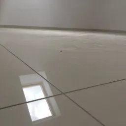 Błyszcząca podłoga z jasnych płytek ceramicznych z widocznymi fugami i odbiciem okna dachowego, niski kąt ujęcia.