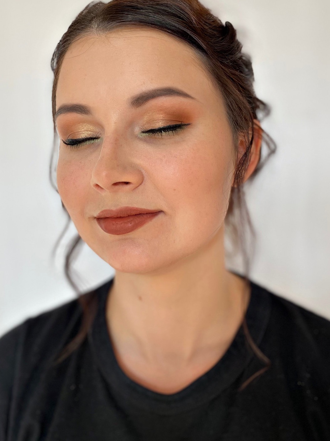 Portret kobiety z zamkniętymi oczami prezentujący makijaż: złote cienie z czarną kreską i brązowa pomadka.