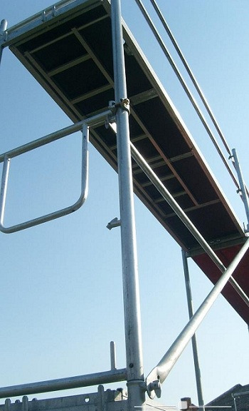 Metalowe rusztowanie z drewnianym pomostem roboczym na tle błękitnego nieba, widok z dołu.