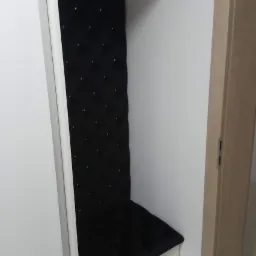 Wnęka z tapicerowanym, czarnym siedziskiem i oparciem z guzikami, wbudowana w białą szafę.