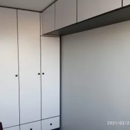 Biała szafa na wymiar z czarnymi uchwytami i cienkimi czarnymi obramowaniami, z g&oacute;rnymi szafkami do sufitu, widok z boku.